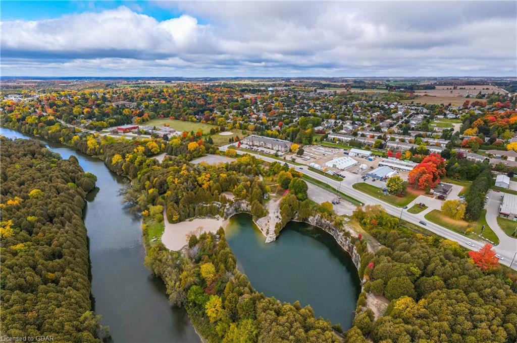 Aerial view of Elora with the Grand River, quarry lake, autumn trees, and surrounding neighbourhoods under a bright, cloudy sky in Ontario.